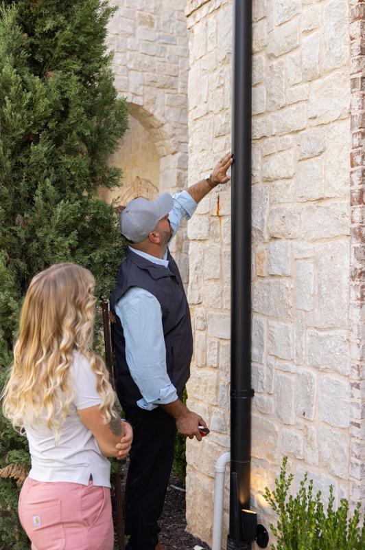 Robert Spence inspecting a downspout with a homeowner